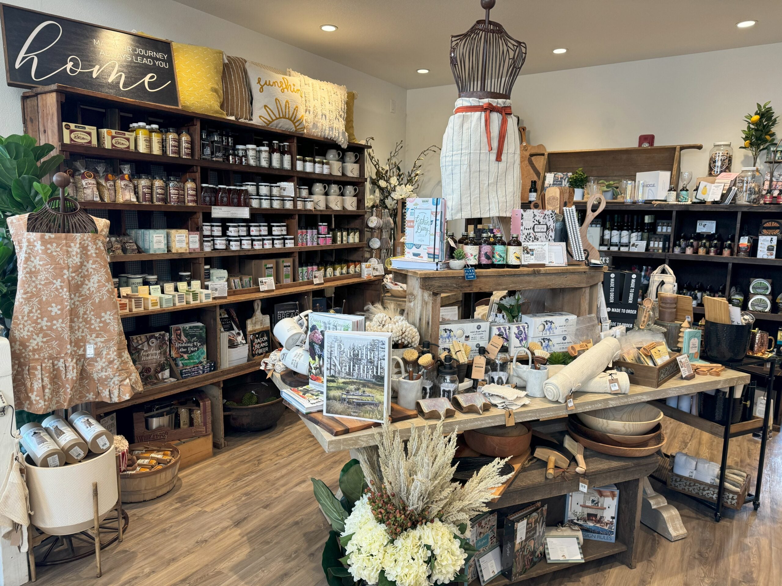 The dahlias themed gift shop has a feature table in the center, with shelves of local and specialty goods on shelves behind