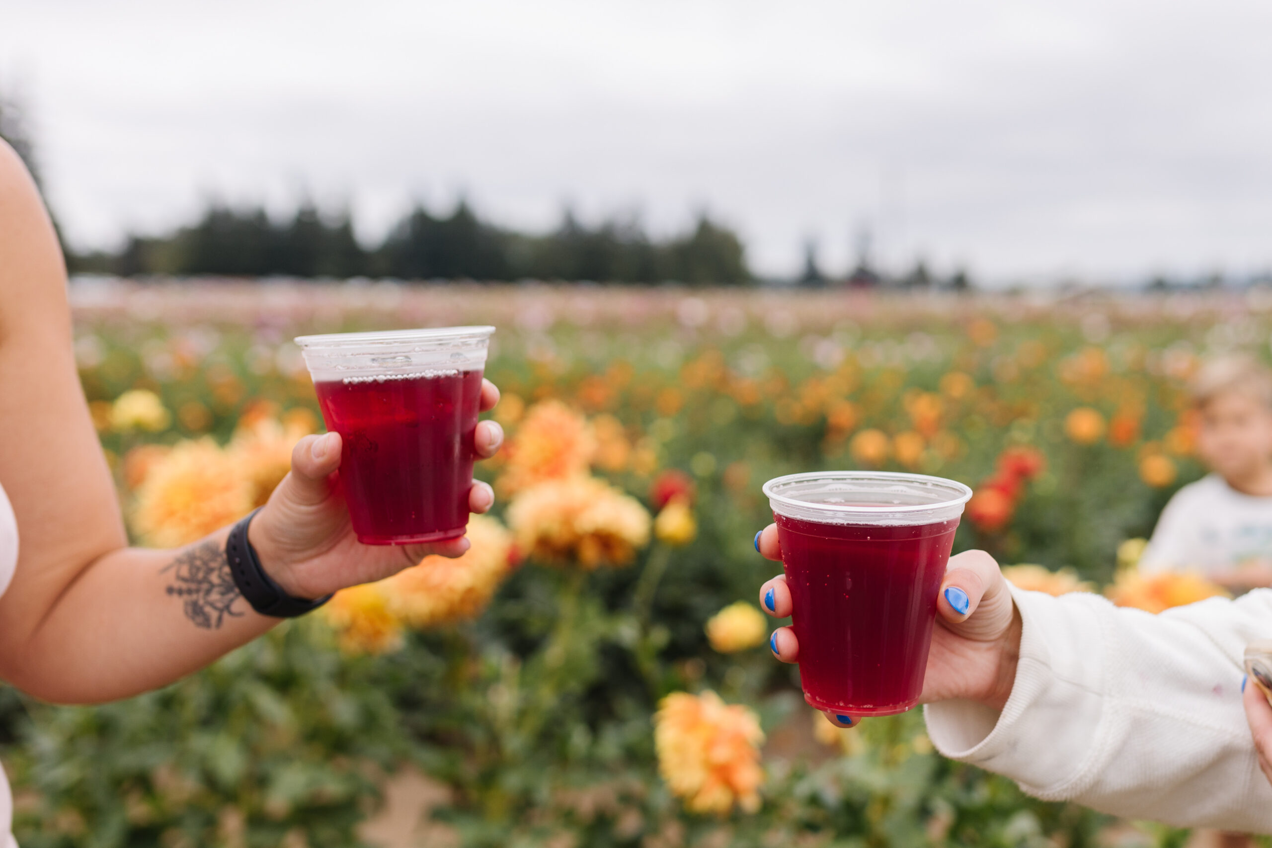 Two people hold cups of red juice, with colorful flowers in the background.
